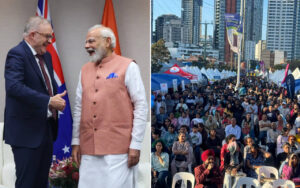 Two men in formal attire shake hands on a stage with flags in the background. One wears a peach vest; the other a dark suit.