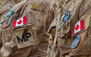 Close-up of Canadian soldiers in camouflage uniforms with medals and patches, including a large MP patch on the sleeve.