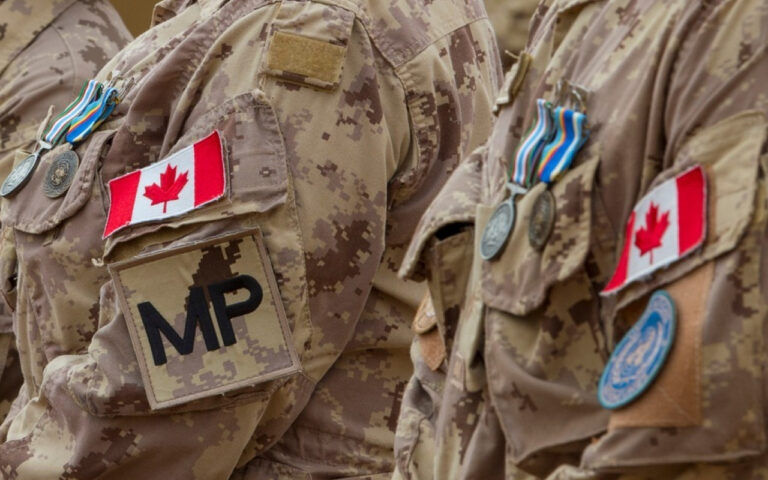 Close-up of Canadian soldiers in camouflage uniforms with medals and patches, including a large MP patch on the sleeve.