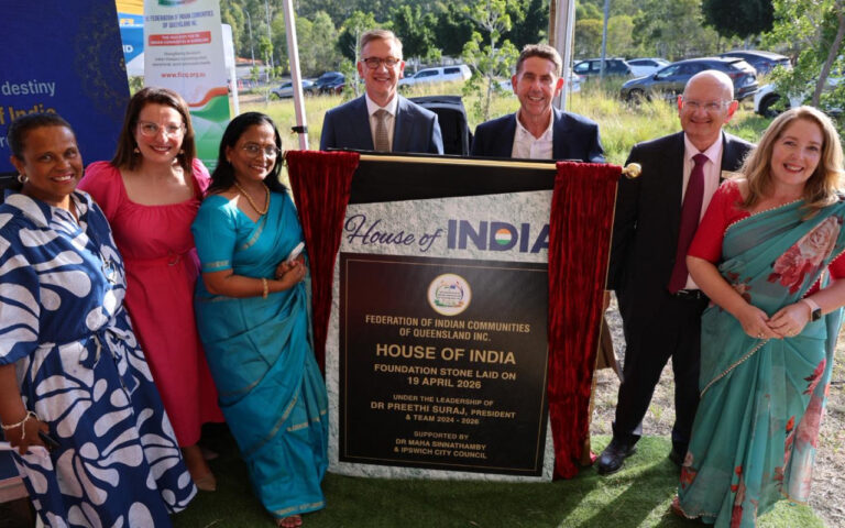 Group of seven people standing beside a commemorative plaque reading 'House of India' during a ceremony outside. (informative)
