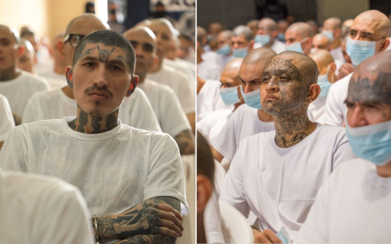 Two tattooed men in white shirts sit among a crowd at an indoor gathering; foreground left has neck and hand tattoos, right has facial ink.