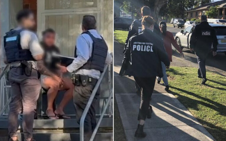 Two officers in tactical vests restrain a seated man on outdoor stairs outside a house, faces blurred or turned away.