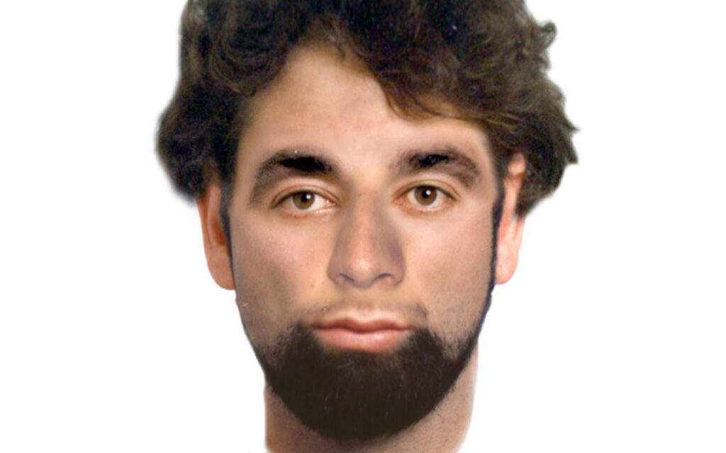 Portrait of a young man with dark hair and a full beard, facing the camera against a white background.