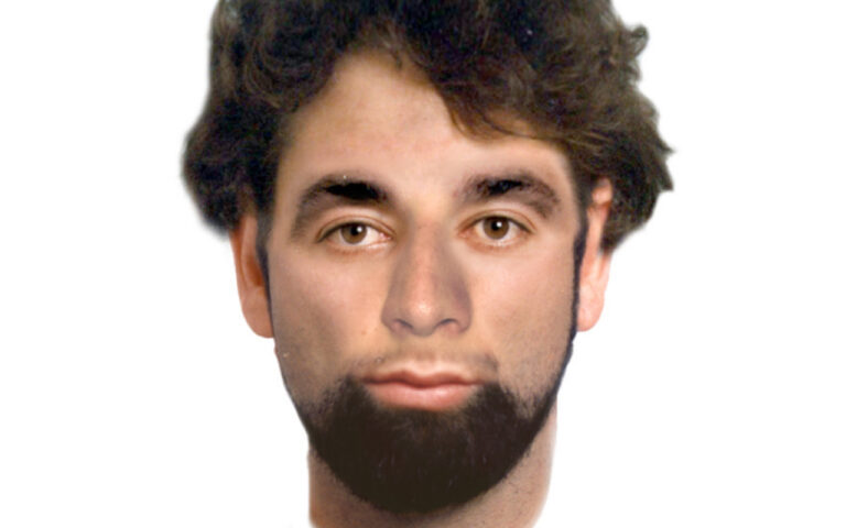 Portrait of a young man with dark hair and a full beard, facing the camera against a white background.