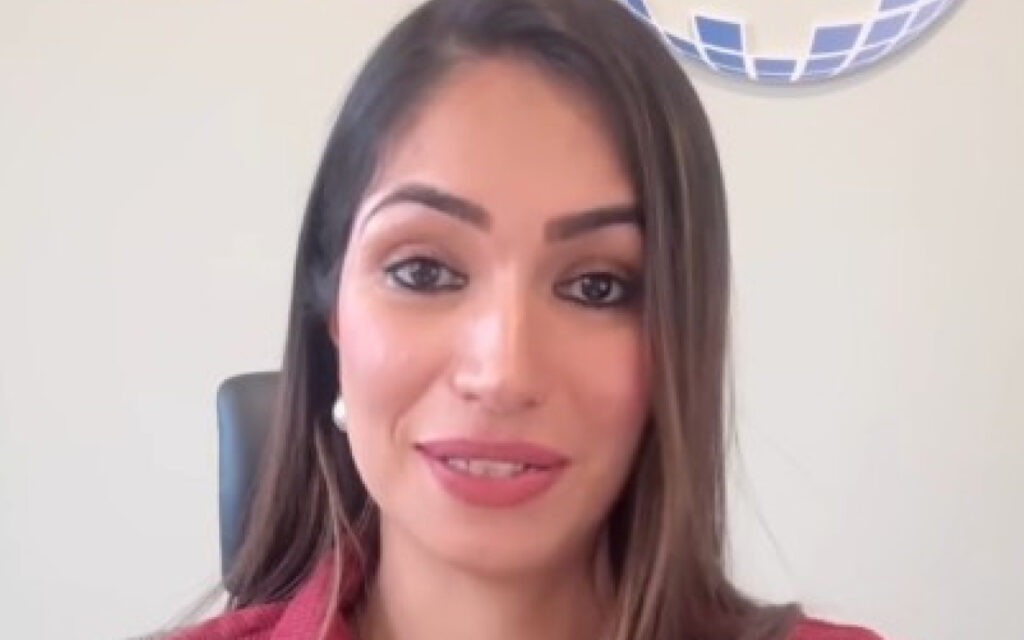 Portrait of a smiling woman with long brown hair, wearing a red top, seated in an office chair.
