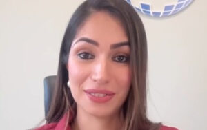 Portrait of a smiling woman with long brown hair, wearing a red top, seated in an office chair.