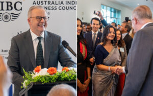 Smiling man in a suit speaks at a podium with orange and white flowers during a formal event; backdrop reads Australian business councilLike text indicating a business gathering.