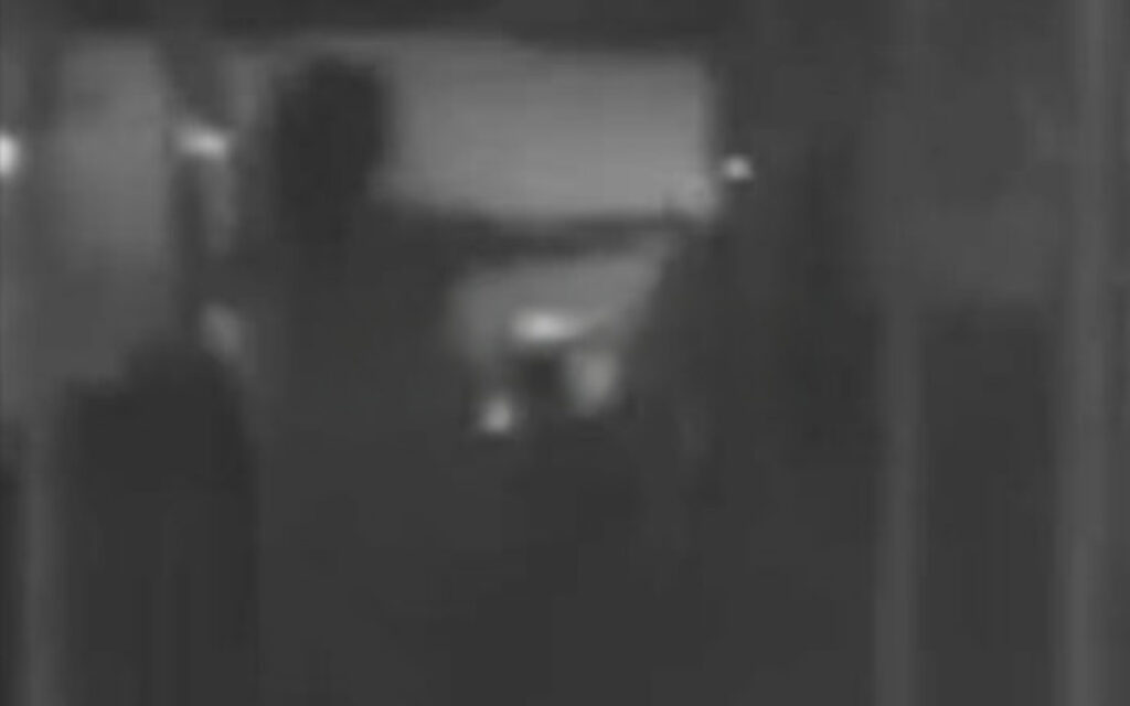 Dim grayscale photo of a dark hallway with a bright rectangular doorway in the center and indistinct shapes nearby.