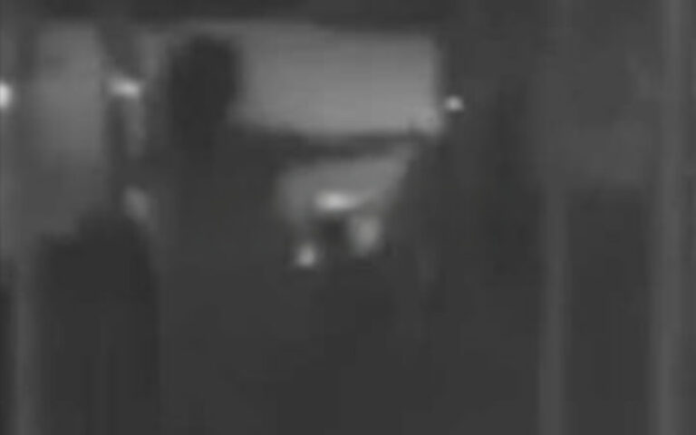 Dim grayscale photo of a dark hallway with a bright rectangular doorway in the center and indistinct shapes nearby.