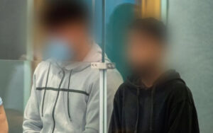 Two people in hoodies stand behind a glass door, their faces blurred for privacy.