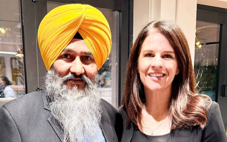 Man wearing a bright yellow turban and gray beard posing with a smiling woman indoors.
