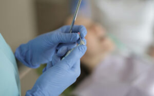 Clinician wearing blue gloves loading a syringe for a dental injection beside a patient lying down.