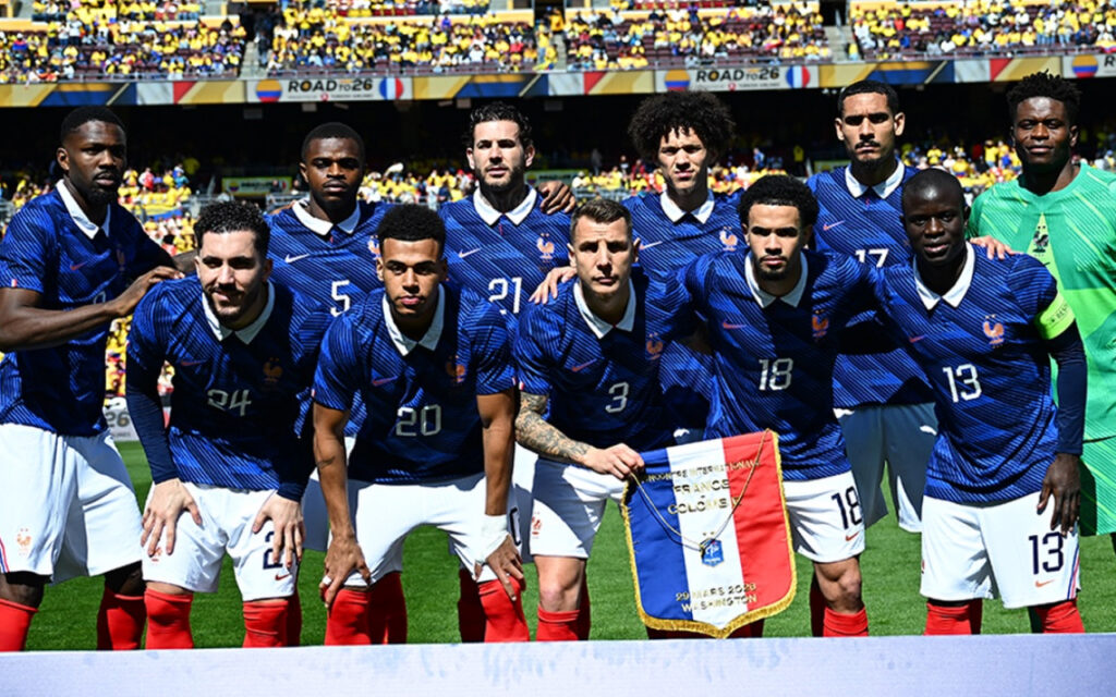 France national football team players pose for a pre-match group photo on the pitch in blue jerseys with white collars and red socks.