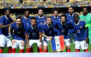 France national football team players pose for a pre-match group photo on the pitch in blue jerseys with white collars and red socks.