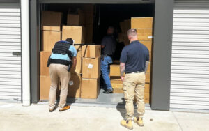 Three men loading large cardboard boxes into an open storage unit.