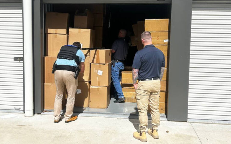 Three men loading large cardboard boxes into an open storage unit.