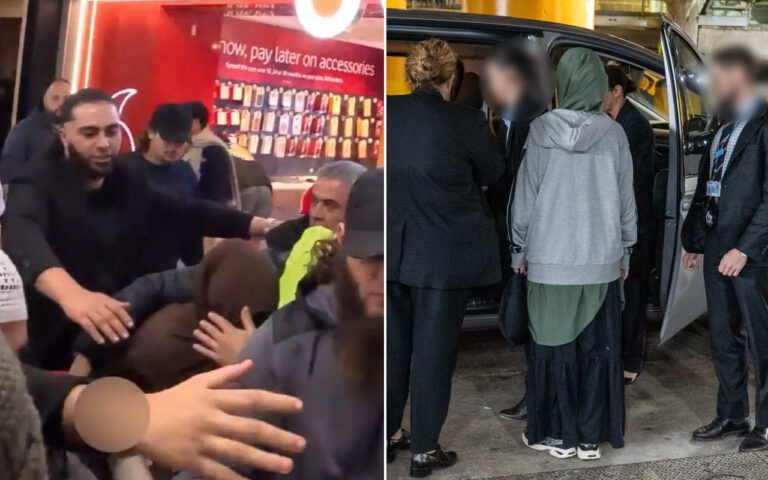 Crowd surrounding a person in a hoodie on a city street at night, with a phone accessory shop sign visible in the background to suggest a busy storefront area.
