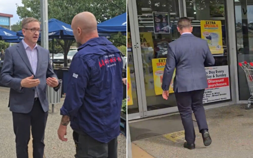 Two men in business attire converse outside a storefront, one facing the other with open hands under a blue canopy setting.