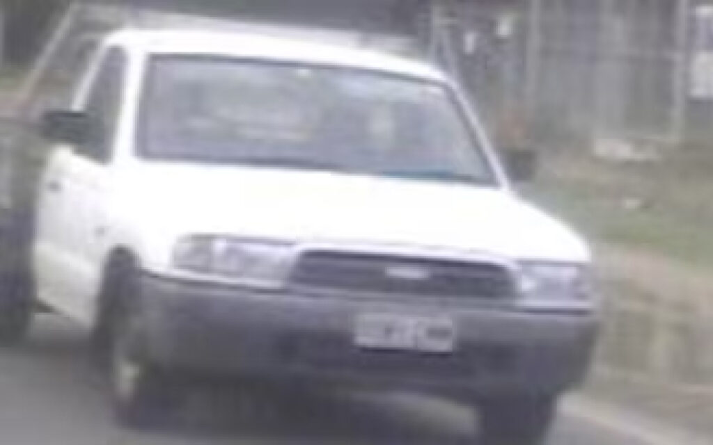 White pickup truck driving toward the camera on a rural road, front view, slightly blurred.