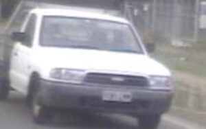 White pickup truck driving toward the camera on a rural road, front view, slightly blurred.