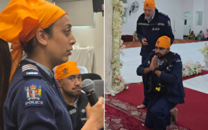 Two police officers at a ceremony: on the left, a female officer in profile with an orange headscarf; on the right, a male officer kneeling in prayer with hands together, another officer behind him.