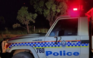 Police vehicle at night with red emergency light on, white SUV marked with blue 'Police' text and checkered stripe.