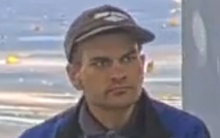 Man wearing a dark cap and blue jacket, looking to the side indoors.