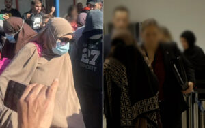 Crowded scene with people wearing masks; a woman in a beige hijab and blue mask is in the foreground, holding a smartphone.