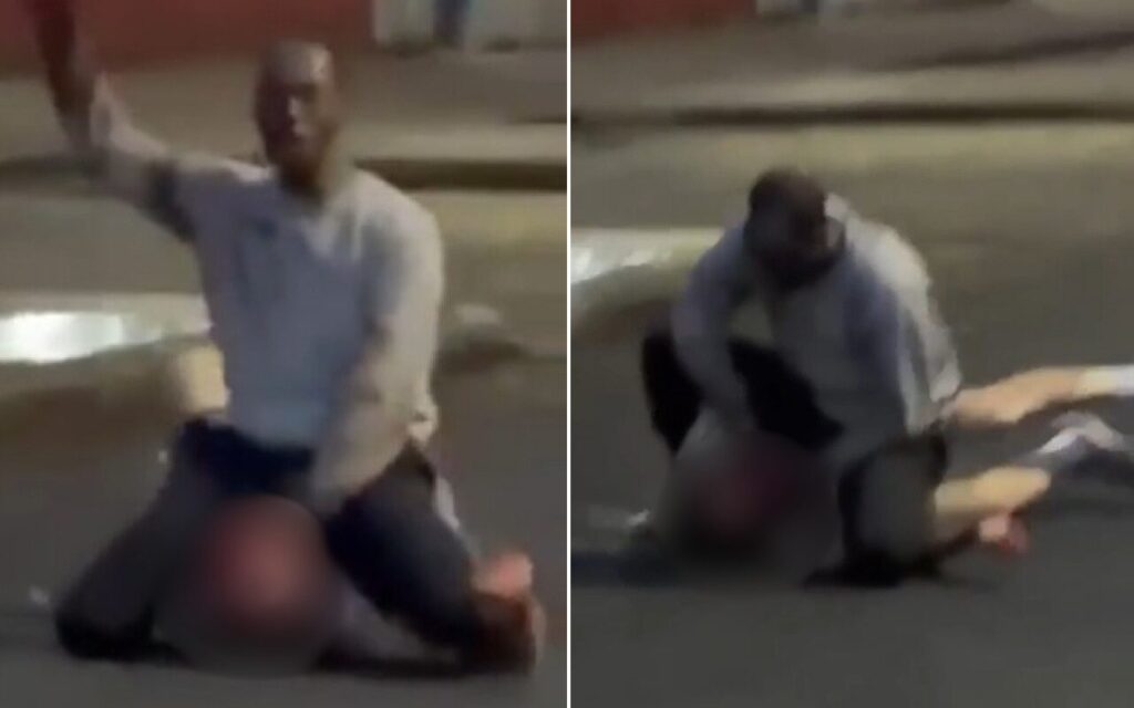 Two men on a dim street at night; one kneels over the other with an arm raised as if threatening or striking.