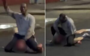 Two men on a dim street at night; one kneels over the other with an arm raised as if threatening or striking.