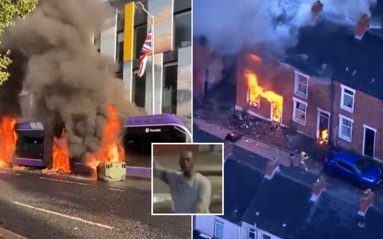 Public transit bus on fire with large flames and smoke on a city street; British flag visible outside a building nearby.