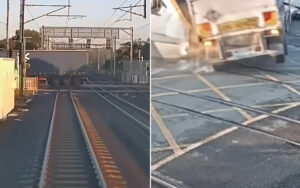 A large semi-truck sits across a railroad crossing, blocking the tracks with overhead wires and crossing equipment nearby.