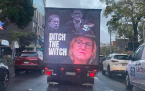Truck with a political ad: 'DITCH THE WITCH' and a woman’s portrait on the back, on a city street.