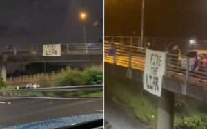 Nighttime scene of a bridge with a banner reading 'FIRE THE LIAR' hanging from the railing.