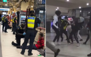 Security officers in high-visibility vests detain a person on the floor at a train station, with a bystander seated nearby in red.