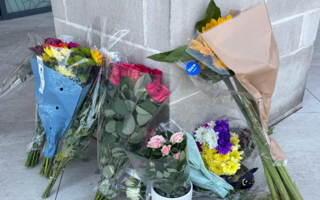 Several flower bouquets wrapped in plastic lean against a concrete wall on a sidewalk near a pillar.