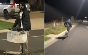 Nighttime scene of a man in a hoodie pushing a large white cooler-like box on a wheeled cart in a parking lot at night.