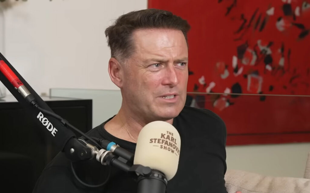 Man in a black shirt speaks into a beige podcast microphone labeled 'The Karl Stefan Show' in a studio setting.