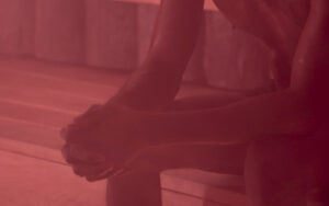 Close-up of a person’s feet in platform sandals resting on a wooden floor with a red tint.