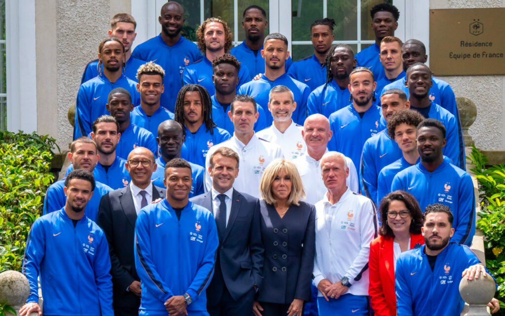 Group photo of France national football team and staff posing outside a building in matching blue jackets with team crest on the left chest.