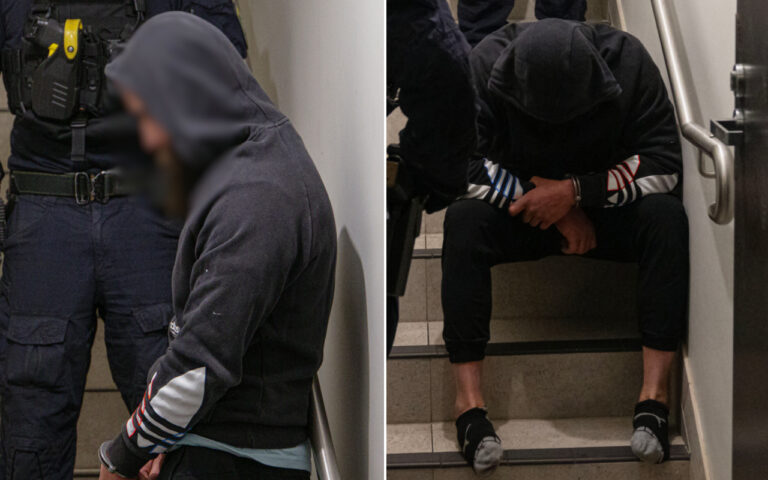 Hooded man with hands cuffed sits on stairs, an officer in tactical gear stands nearby in a doorway scene.