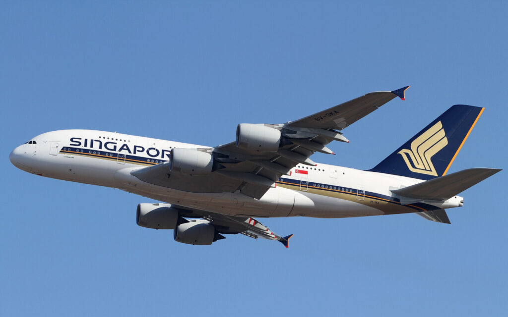 Singapore Airlines Airbus A380 in white and blue livery with four engines, flying left to right against a clear blue sky.