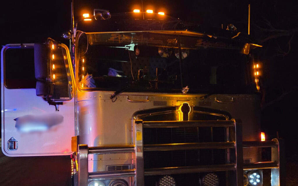 Front view of a white semi-truck at night, with orange roof lights and the driver-side door open.