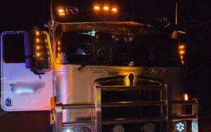 Front view of a white semi-truck at night, with orange roof lights and the driver-side door open.