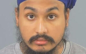Mugshot of a man with a blue headwrap and a beard, facing the camera against a gray backdrop.