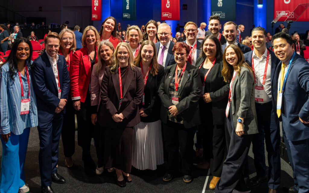 Diverse group of conference attendees in business attire posing for a group photo with red lanyards.