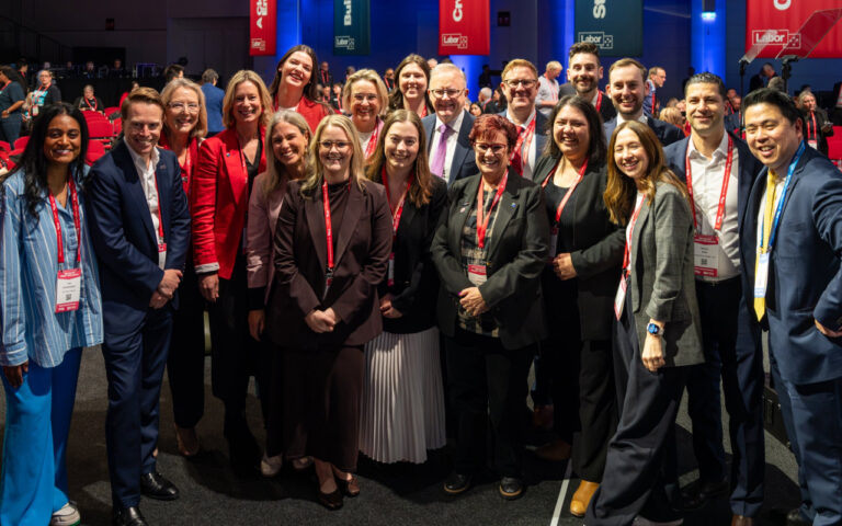 Diverse group of conference attendees in business attire posing for a group photo with red lanyards.