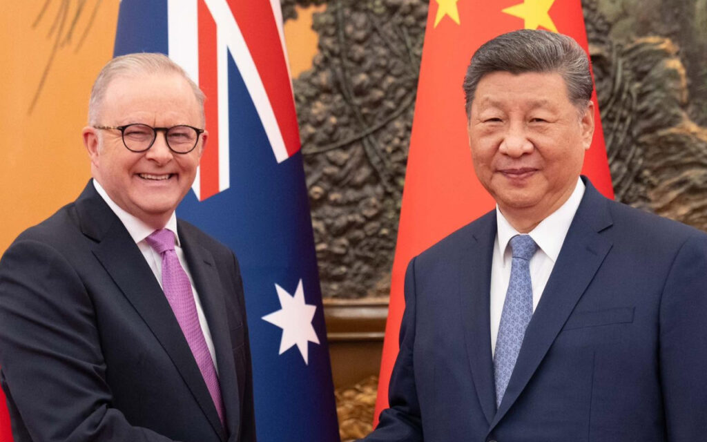 Two men in suits smiling for a formal photo with Australian and Chinese flags in the background.