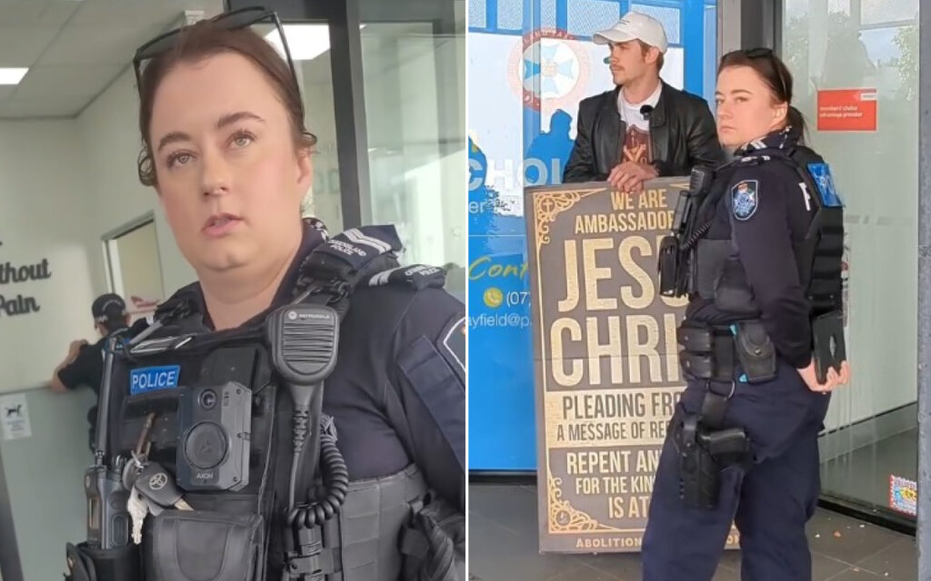 Two police officers in tactical gear indoors; one in the foreground with a radio and body camera, another beside a protest poster by a doorway.