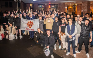 Large group photo of protesters holding a white banner reading 'Jesus Is King' with red crosses, raising rosaries and fists.